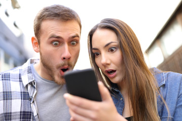 Surprised couple checking online news on smart phone