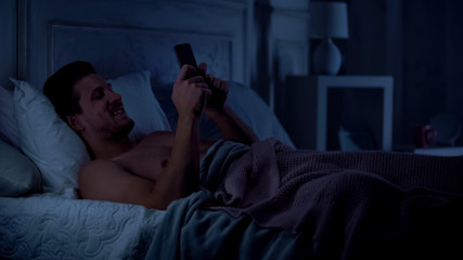 Fototapeta premium Young male texting on smartphone and smiling, chatting with girlfriend, gadget