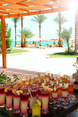 Tasty cocktails in background of tropical resort with palm trees, sea and people