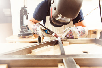Male in face mask welds with argon-arc welding