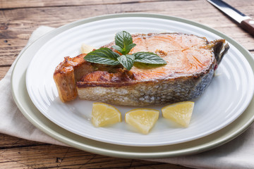 Steak baked fish salmon on a plate with lemon. Wooden table.