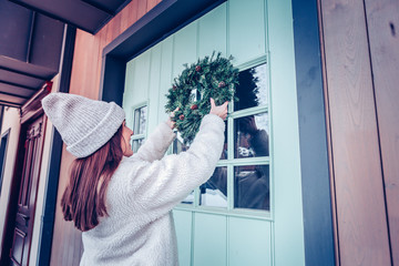 Woman with long dark hair putting Christmas wreath on front door © Viacheslav Yakobchuk