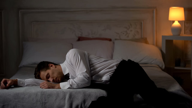 Overworked Tired Man In Suit Lying Down On Bed In Exhaustion, Single Workaholic