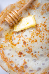 A stack of thin russian pancakes with butter and honey on a white plate