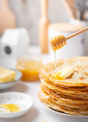 A stack of thin russian pancakes with butter and honey on a white plate
