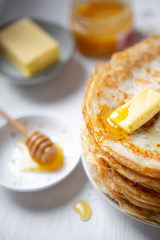 A stack of thin russian pancakes with butter and honey on a white plate