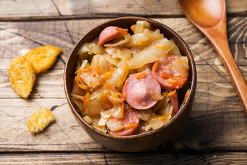 Stewed cabbage with sausages in wooden bowls on the table. Selective focus.