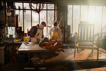 Fototapeta na wymiar A craftsman in his workshop teaches his work to his apprentice