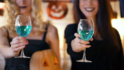 Two ladies in costumes showing blue beverages, all saints night celebration