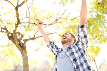 Excited guy celebrating success raising arms in a park