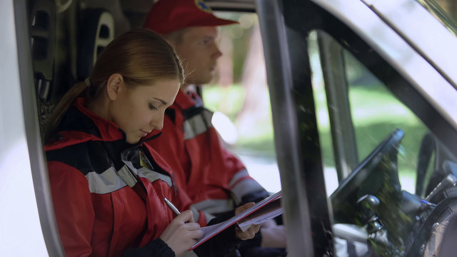 Paramedic writing report in ambulance, professionals on duty, emergency services
