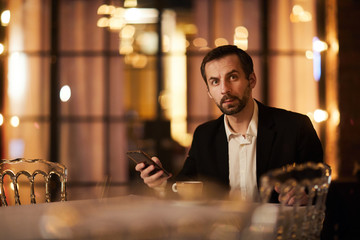 Portrait of mature businessman holding smartphone enjoying evening in cafe, copy space