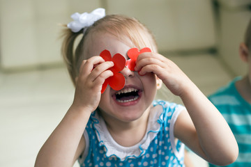 cute smiling baby 3 years old blonde-haired, blue-eyed shears out paper and sticks on paper