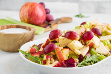 Waldorf salad with apples, celery, grapes, walnuts and arugula on white plate