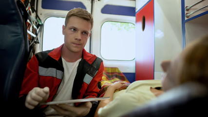 Paramedic asking patient questions and filling out medical form in ambulance