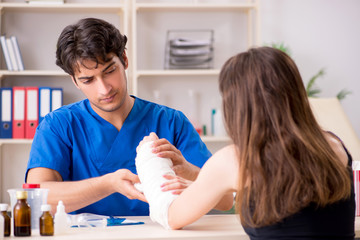 Young woman with bandaged arm visiting male doctor traumotologis