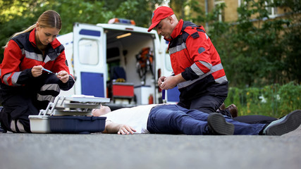 Paramedics helping unconscious man on road, making injection with insulin