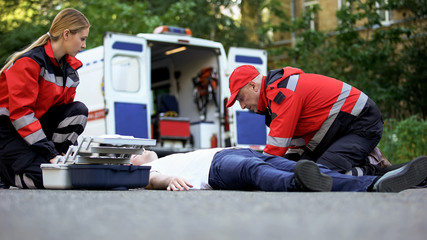 Ambulance crew helping unconscious man on road, first aid at car accident scene