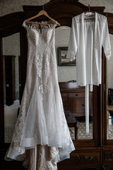 White wedding gown and a white pyjamas are hanging on a cabinet with mirror.