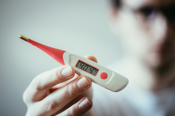 Man is holding a fever thermometer in his hand, blurry face