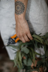 Hand of a young woman with a tatoo closeup. She is holding the secateurs and a plant at her hand.