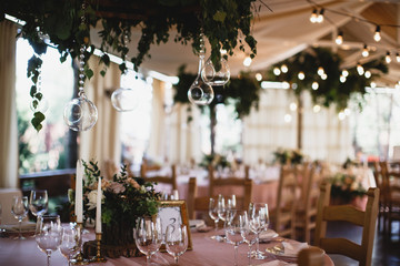A table with a lots of wineglasses and a flower bouquet on it. Restauraunt terrace at the background.