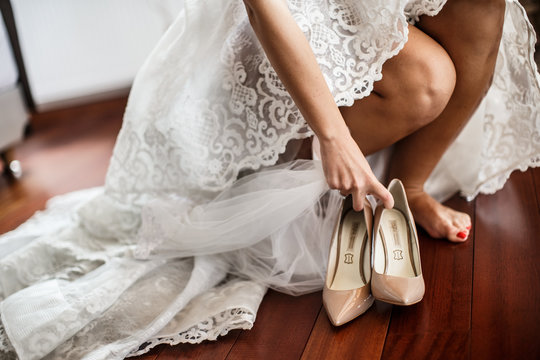 A bride puts on the high heels. She is wearing a wedding dress. Wedding preparation concept.