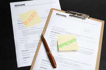 Two resume templates and sticks on it, black background. HR made decision and approved one...
