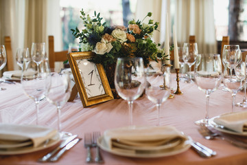 A lots of cutlery and some wineglasses are standing on the table. There is a flower bouquet at the middle of the table.
