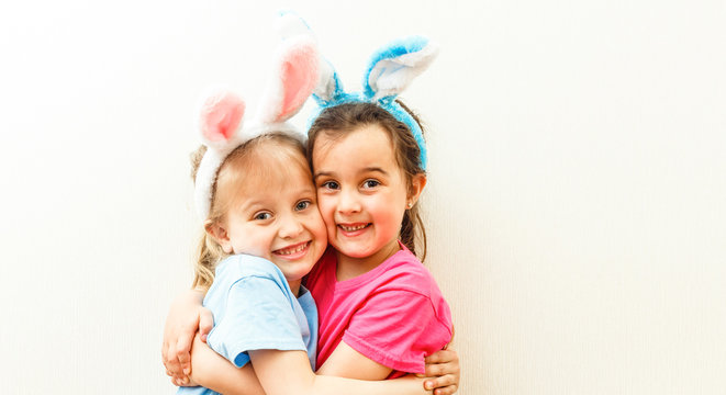 Two cute little sisters wearing bunny ears playing egg hunt on Easter. Adorable children celebrate Easter at home.