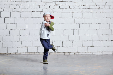 Child boy dancing. Cool kid hip hop break dancing on brick wall background. Little man movement,...