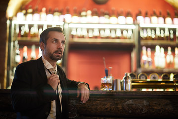 Portrait of handsome mature man sitting at bar counter and loosening his tie, copy space