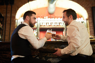 Side view portrait of two business people drinking whiskey at bar counter celebrating successful...