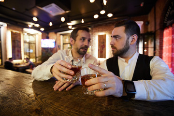 Portrait of two business people drinking whiskey at bar counter celebrating successful deal after work, copy space