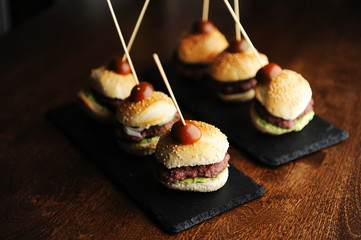 Mini beef burgers on black slate boards. Sesame buns. Dark background