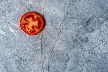 Obraz na płótnie Canvas Single slice of red tomato from above on the marble background with copy space
