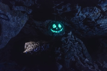 Dark creepy glowing phosphorescent smiling face on hanging stone in cave