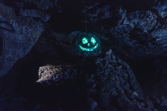 Dark creepy glowing phosphorescent smiling face on hanging stone in cave