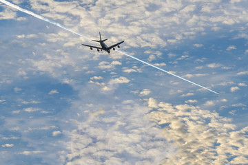 Landscape with the white airplane is flying in the blue sky over the clouds