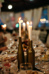 Three candles standing in the middle of a table alongside with a lots of food and cutlery.