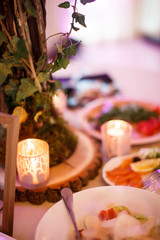 A decorative tree is standing at the middle of a table alongside with some cutlery and a pair of candles.