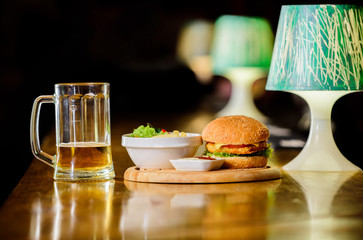High calorie snack. Hamburger and french fries and tomato sauce on wooden board. Delicious burger. Burger with cheese meat and salad. Pub food and mug of beer. Fast food concept. Burger menu