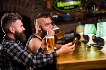 Men drinking beer together. Hipster brutal man drinking beer with friend at bar counter. Men drunk relaxing having fun. Alcohol drinks. Friends relaxing in pub with beer. Refreshing beer concept