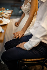 A groom and a bride are holding hands. They are sitting behind the table.