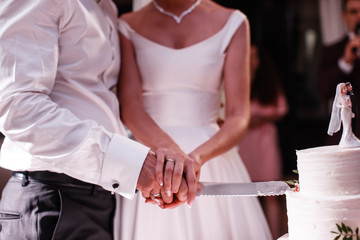 The bride and the groom are cutting the white wedding cake with a knife closeup.
