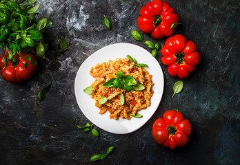 Tasty pasta with minced meat and tomato sauce with green basil on white plate, dark background kitchen table, top view