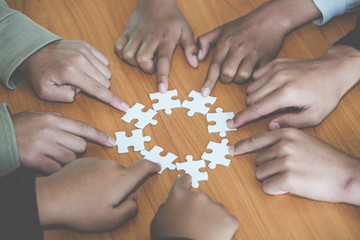people helping in assembling puzzle, cooperation in decision making, team support in solving problems and corporate group teamwork concept, close up view of hands connecting pieces