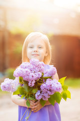 Obraz na płótnie Canvas smiling little cute blonde girl with a bouquet of lilac in the hands in the lilac dress