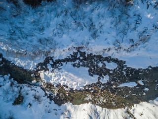 Aerial view of snow covered stones in river flowing through winter landscape from above.