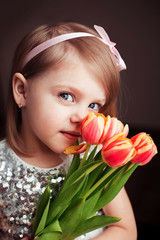 Obraz na płótnie Canvas cute little blonde girl of three years with peach tulips close-up, smiling, look into the camera, vertical photo